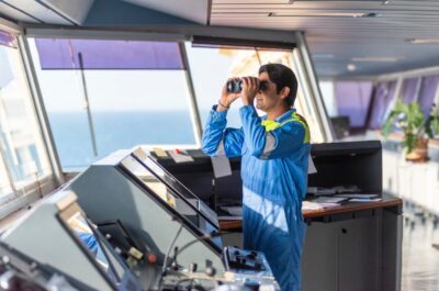 Chief officer on the bridge of a merchant ship, wearing a light blue uniform with epaulettes, working with pride and confidence - an authentic portrait of leadership at sea. Real workplace.