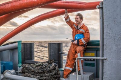 Marine Deck Officer or Chief mate on deck of offshore vessel or ship , wearing PPE personal protective equipment - helmet, coverall. He is smiling